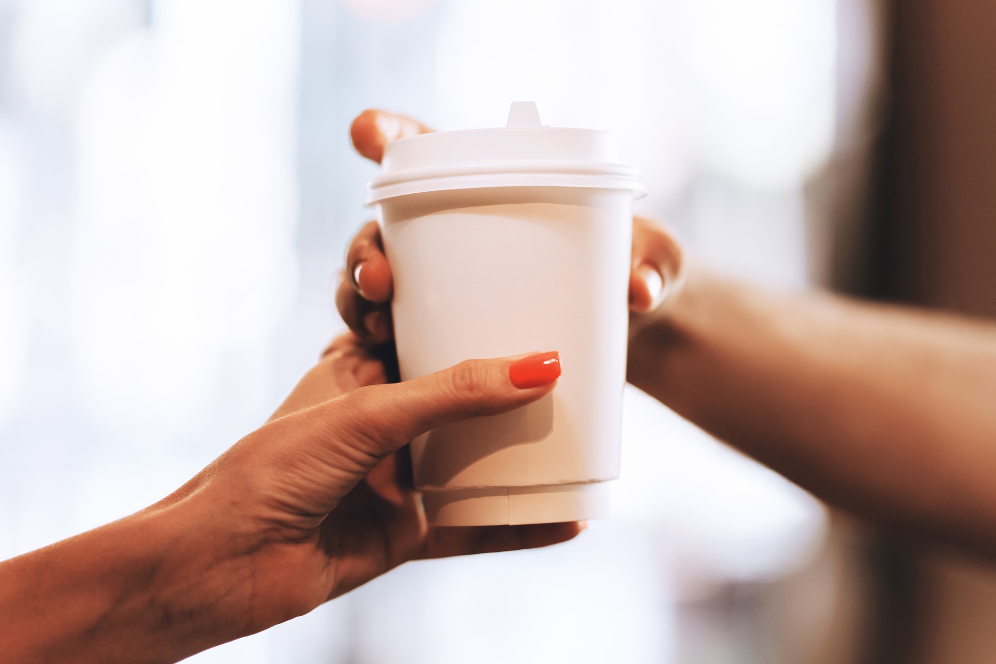 Barista passes coffee to a visitor in a popular coffee shop, hands and a glass of coffee are shot