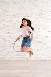 Girl playing with hula hoop in bright room