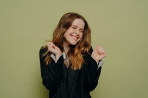 Happy young woman with closed eyes holding hands up with excitement