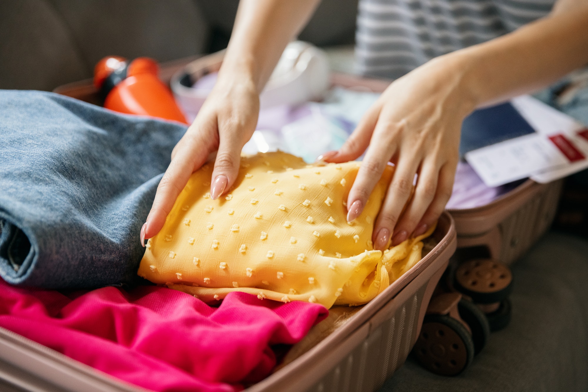 Close-up female hands packing suitcase for summer vacation, holiday at home interior, indoors